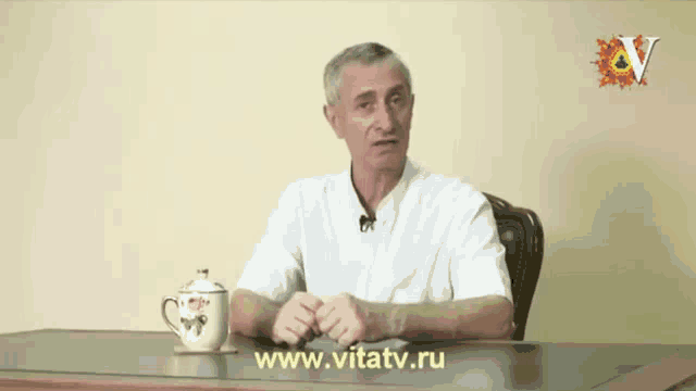 a man sits at a desk with a cup of tea and the website www.vitatv.ru displayed