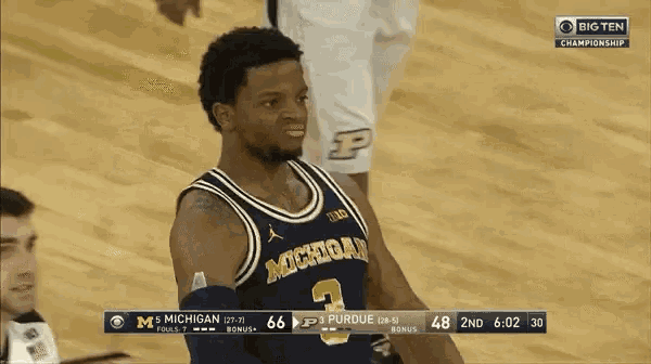 a basketball player wearing a michigan jersey stands on the court during a game