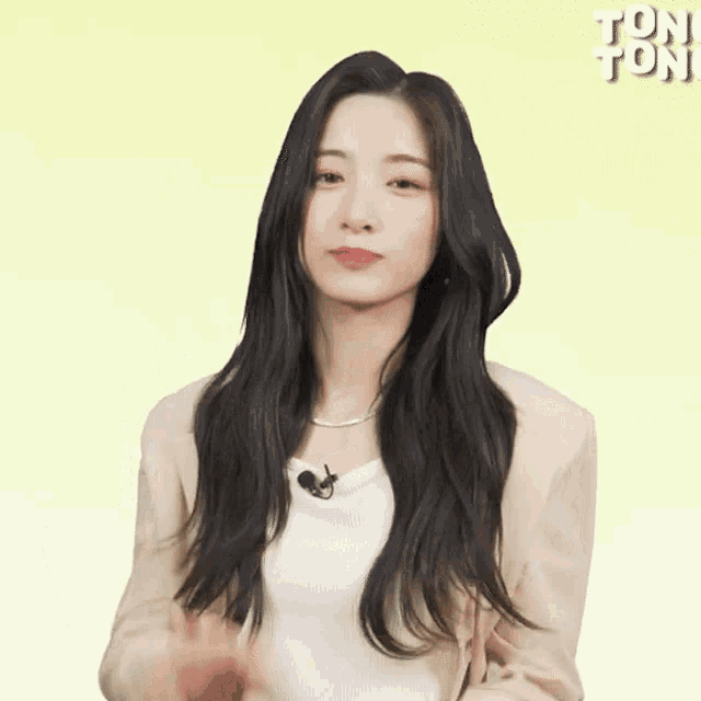 a woman with long black hair wearing a white shirt and a tan jacket