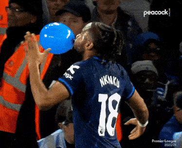 a soccer player blowing up a blue balloon while wearing the number 18 jersey