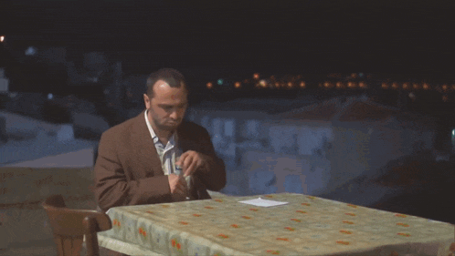 a man sits at a table drinking from a glass at night
