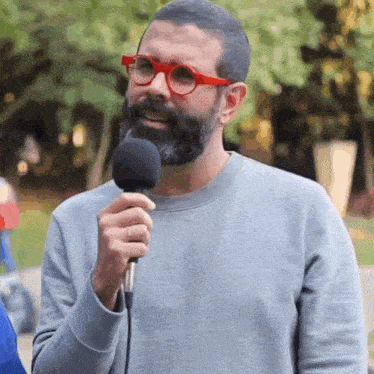 a man with a beard and red glasses holds a microphone