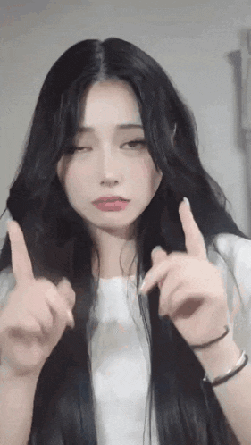 a woman with long black hair is making a funny face while pointing her fingers up .