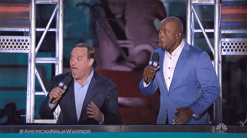 two men standing on a stage with microphones in front of a sign that says #americanninjawarrior