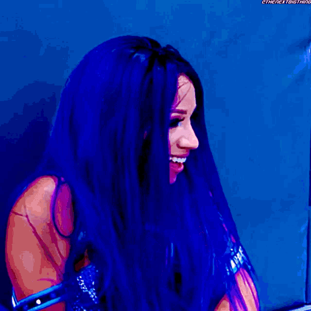 a woman with long blue hair is smiling and wearing a black bra .