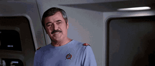 a man with a mustache is wearing a blue shirt with a star trek logo on the front