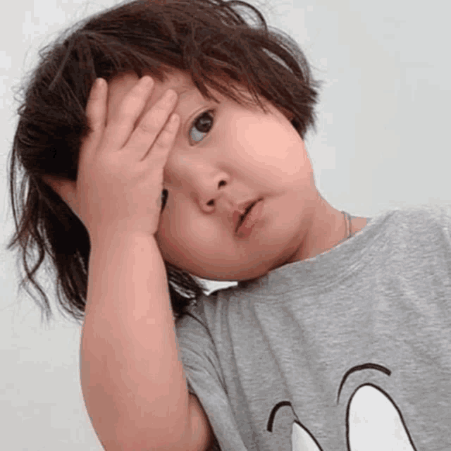 a little girl covering her face with her hand and wearing a gray shirt