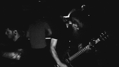 a man is playing a keyboard in a dark room while another man stands behind him .
