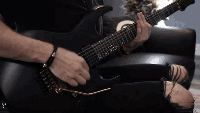 a man is playing a black electric guitar with a gold bridge