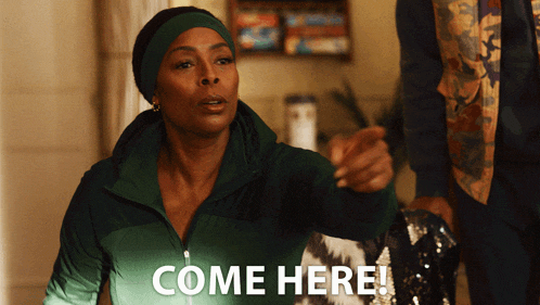a woman in a green jacket says come here while pointing at something