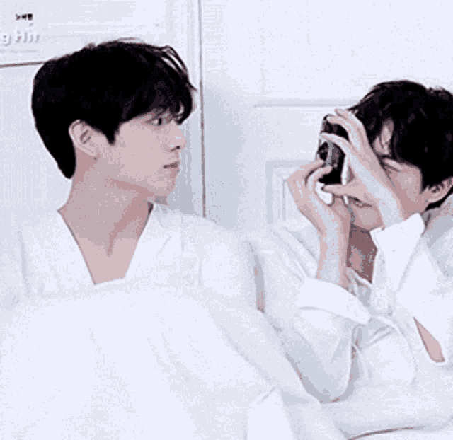two men are laying in bed and one is taking a picture of the other
