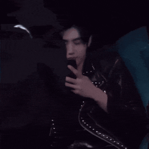 a woman in a leather jacket is sitting on a couch looking at her phone