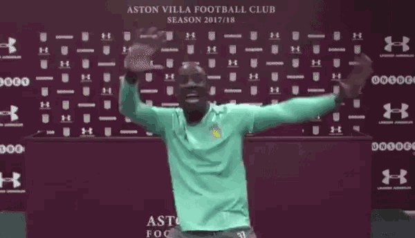 a man in a green shirt is standing in front of a wall with his arms outstretched and smiling .