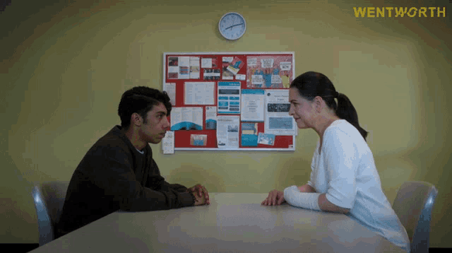 a man and woman sit at a table in front of a bulletin board that says wentworth on it