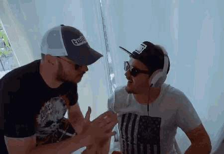 a man wearing a hat that says twitch talks to another man