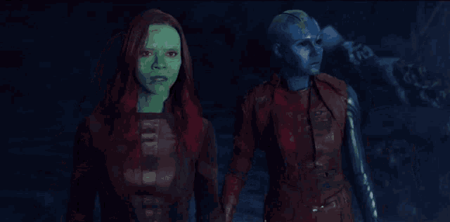 a woman with green hair and a blue face is standing next to a woman with red hair .