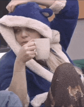 a woman in a blue robe is drinking a cup of coffee .