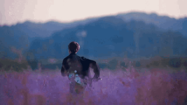 a man in a kimono is walking through a field of purple flowers