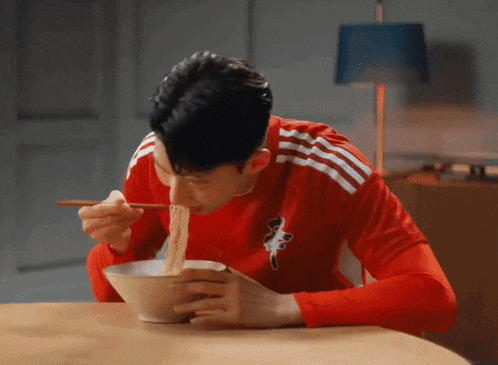 a man in a red adidas shirt eating noodles with chopsticks