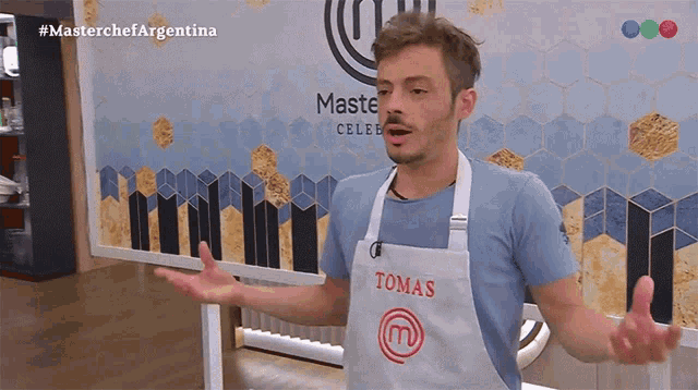 a man wearing a tomas apron stands in front of a masterchef argentina sign