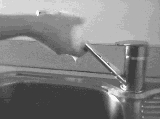 a black and white photo of a person using a faucet