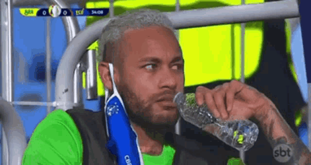 a man is drinking water from a bottle while sitting in the stands .