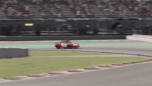 a red race car with a white stripe on the side is driving on a track