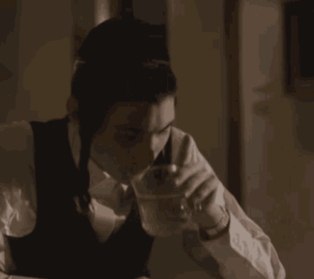 a man in a suit is sitting at a table with a glass of water and a spoon in his hand .