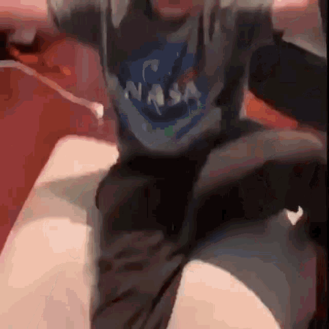 a man wearing a nasa shirt and black shorts is sitting on a bed .