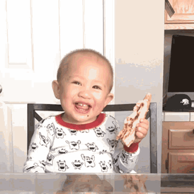 a baby is sitting at a table holding a slice of pizza