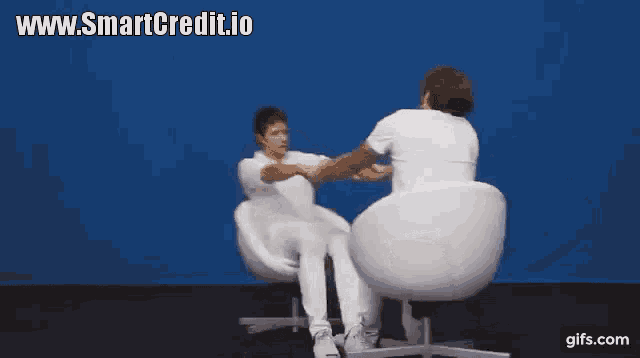 two men are shaking hands while sitting in white chairs with a blue background .