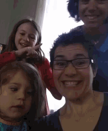 a woman wearing glasses and a necklace smiles with two young girls