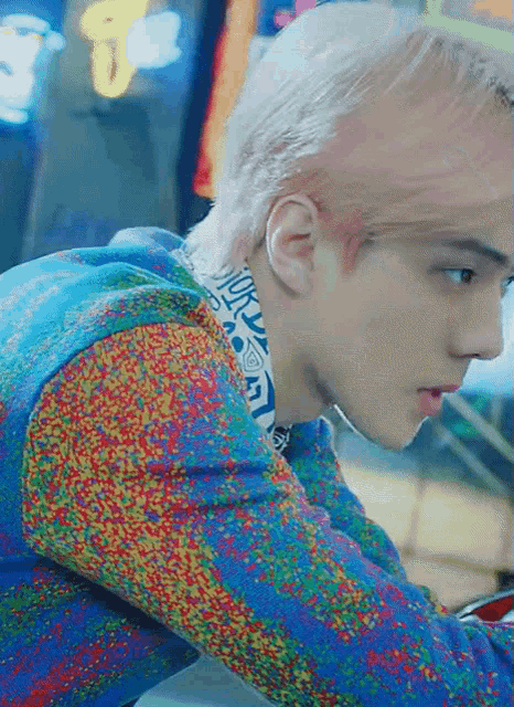 a man with white hair is wearing a colorful sweater and playing a video game
