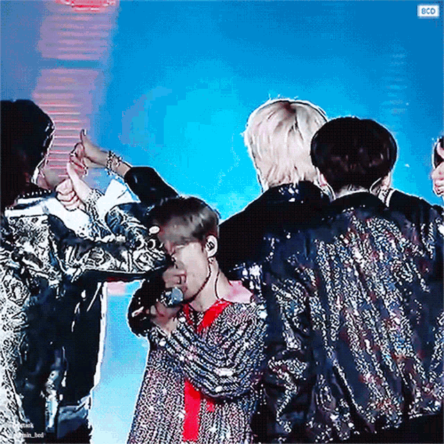 a group of people are on a stage and one of them is wearing a sequined jacket and holding a microphone