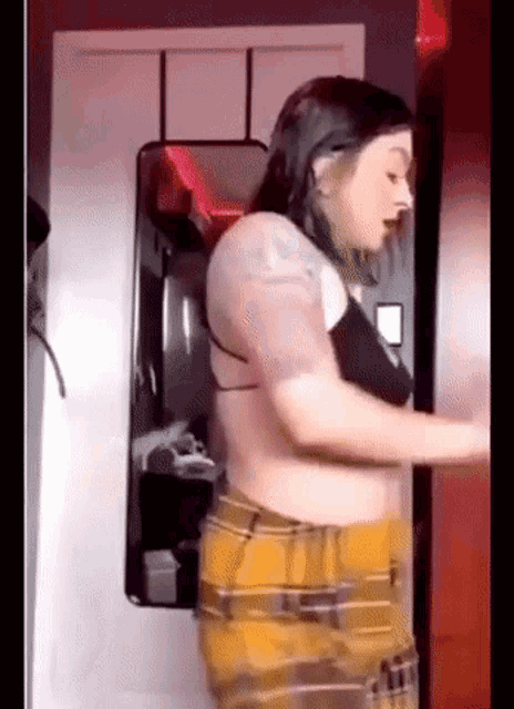 a woman is standing in front of a mirror wearing a bra and plaid shorts .