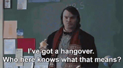a man is standing in front of a blackboard eating a sandwich and talking about having a hangover .