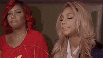 two women are sitting next to each other on a chair . one of the women has red hair and the other has blonde hair .
