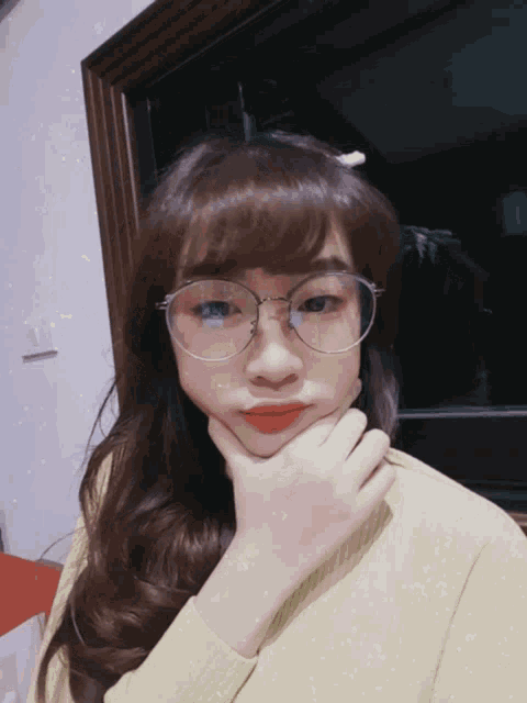 a girl wearing glasses and a green sweater holds her chin