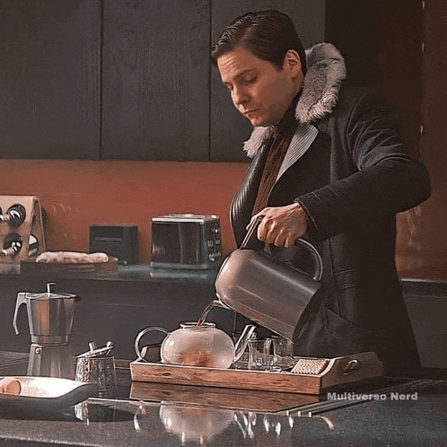 a man is pouring water into a teapot on a tray on a kitchen counter .