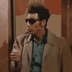 a man wearing sunglasses and a brown coat is giving a thumbs up .