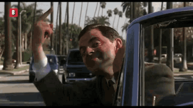 a man in a suit and tie is pointing out of a car window with the letter b above him