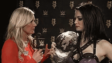 two women are standing next to each other and one is holding a wrestling championship .