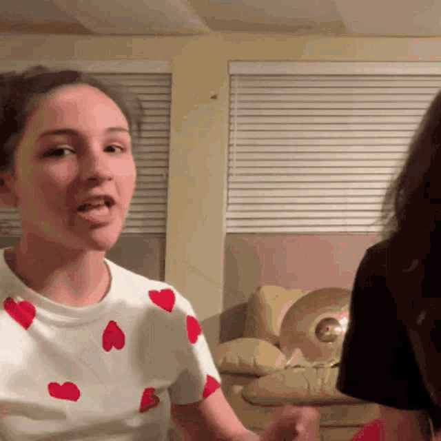 a woman wearing a shirt with red hearts on it is talking to another woman