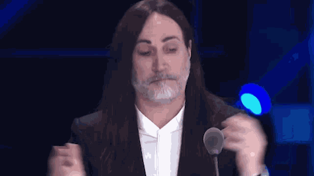 a man with long hair and a beard is standing in front of a microphone and making a funny face .