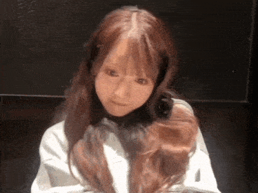 a young woman with long red hair is sitting in a dark room and looking at the camera .