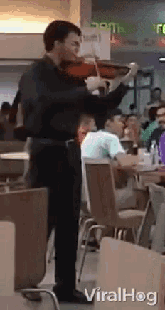 a man is playing a violin in a restaurant while people sit at tables .