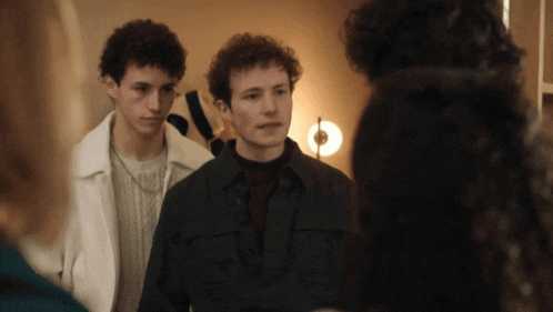 two young men are standing next to each other in a room with a woman in the foreground
