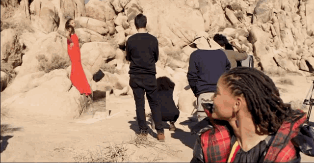 a woman in a red dress is being photographed by a group of people in the desert