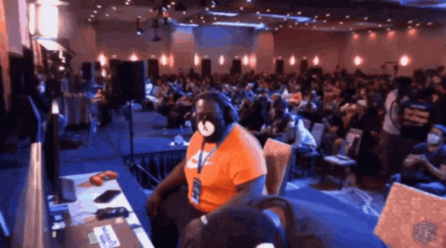 a man wearing an orange nike shirt sits in front of a crowd of people