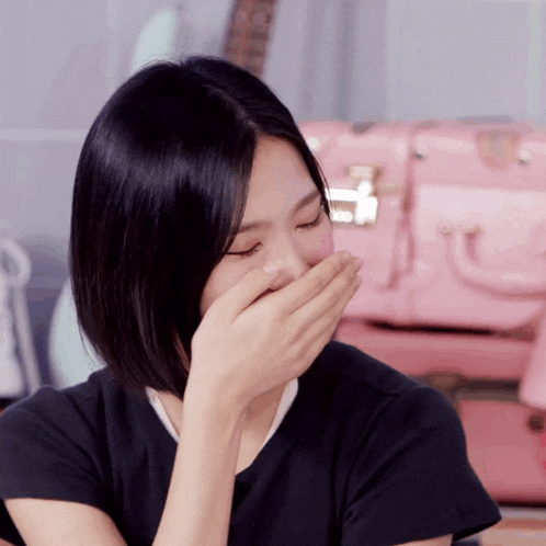 a woman is covering her mouth with her hand in front of a pink bag